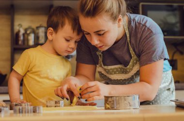 Mutfakta mutlu bir aile. Anne ve çocuk hamuru hazırlıyor, kurabiye pişiriyor. Mutfakta aile eğlencesi kavramı, çocuk çeşitli yemekler hazırlıyor: makarna, kurabiye, ekmek, zencefilli ekmek.. 