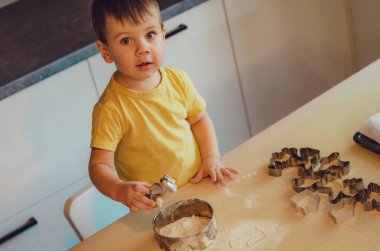 Küçük tatlı çocuk, ev mutfağında pasta yapmayı öğreniyor. Mutfakta aile eğlencesi, çocuk yemek hazırlama, çeşitli yemekler: makarna, kurabiye, ekmek, zencefilli ekmek. Klasik renk tonu. 