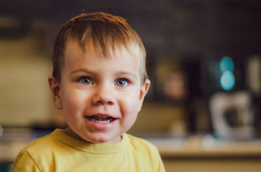 Büyük gözlü, çekici görünümlü sarı tişörtlü güzel bir çocuk. Gülümsüyor, odasında ve mutfakta hediyeler veriyor.