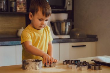 Evde mutfakta yemek pişiren sevimli çocuk. Mutfakta aile eğlencesi kavramı, çocuk çeşitli yemekler hazırlıyor: makarna, kurabiye, ekmek, zencefilli ekmek..