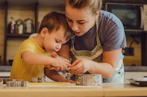 Sevimli küçük oğlan ve önlüklü güzel annesi mutfakta hamuru yoğururken gülüp oynuyorlar..