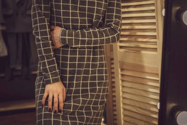 Güzel vücutlu bir kadın, kadın kıyafetlerinin bulunduğu şık bir galeride sıkıca sarılmış bir elbise giymiş büyük bir aynanın önünde poz verir. Başsız fotokopi, sadece gövde