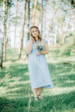 Mavi elbiseli güzel sarışın bir kadın güneşli bir havada parkta yürür. Güzel bir kız gülümsüyor.