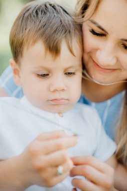 Anne, fotoğrafçıya poz vermesi için oğlunu fotoğraf çekiminde tutuyor. Yeşil doğada mutlu bir aile.