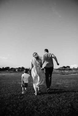 Mutlu genç aile dışarıda yeşil doğada birlikte vakit geçiriyor.