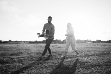 Mutlu genç aile dışarıda yeşil doğada birlikte vakit geçiriyor.