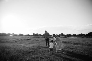 Mutlu genç aile dışarıda yeşil doğada birlikte vakit geçiriyor.