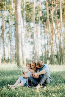 Mutlu genç aile dışarıda yeşil doğada birlikte vakit geçiriyor.