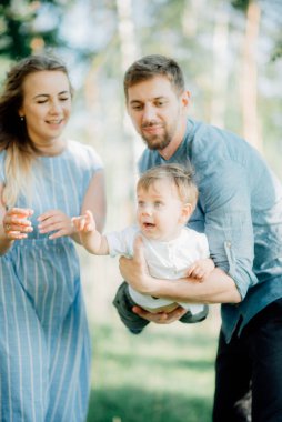 Mutlu genç aile dışarıda yeşil doğada birlikte vakit geçiriyor.
