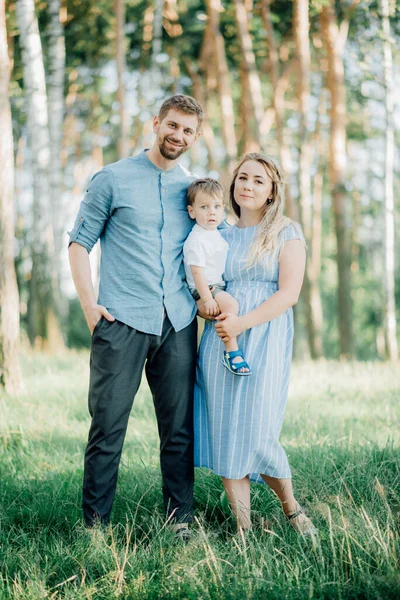 Mutlu genç aile dışarıda yeşil doğada birlikte vakit geçiriyor.