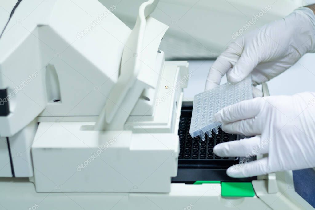 Researcher or scientific introducing a 96 wells plate in quantitative PCR machine/ Thermocycler for DNA or RNA quantification in a biotechnology laboratory