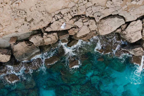 Newlyweds lie on the rocks against the background of the turquoise sea.  Aerial photography