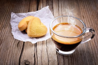 Cam bir fincanda buharlı espresso, eski ahşap bir arka plan ve iki kalp şeklinde bisküvi..