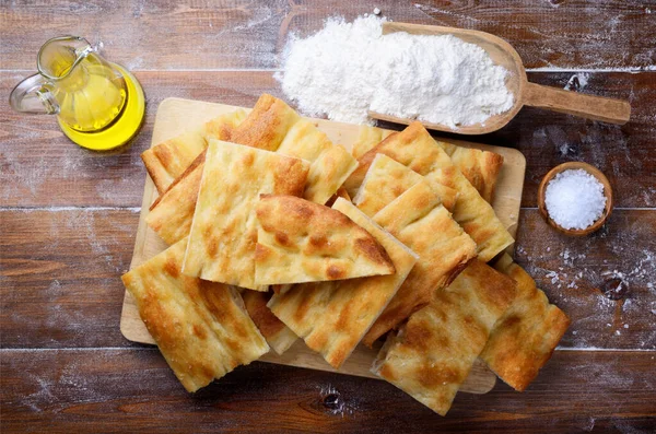 Focaccia ekmeği, düz ekmek, doğrama tahtası, zeytin yağı, un ve ahşap kaplama üzerine tuz, Üst Manzara.