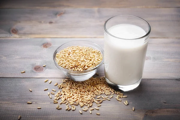 Glass of oat milk with oat seeds on wooden background.