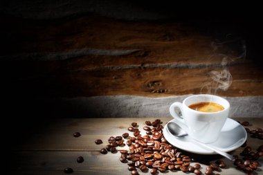 Buharda pişmiş espresso fincanı ve kahve çekirdekleri ahşap masada..