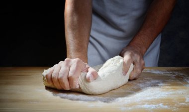 Elleri ekmek ya da pizza hamurunu tahta bir pasta tahtasında yoğurur..