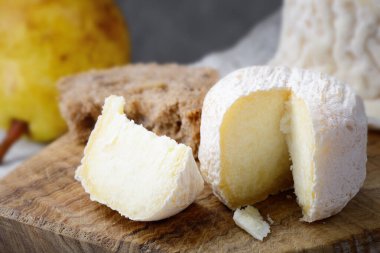 Crottin de Chavignol, French goat cheese on chopping board with bread an pear, selective focus. clipart