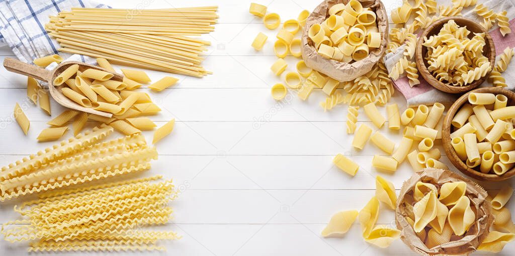 Assorted raw pasta: pens, shells, rigatoni, fusilli, linguine, and squid, top view, copy space. 