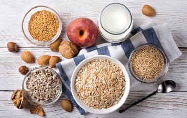 Beyaz ahşap zemin üzerinde yulaf, keten tohumu, ayçekirdeği, susam tohumu, süt, elma, ceviz, badem ve fındık ile kahvaltı..