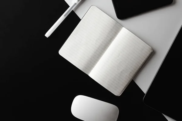 Flat lay tablet, computer mouse and phone with notebook and pencil on a black and white split background