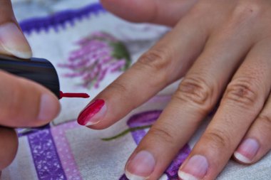 Tırnaklarını fırçayla kırmızıya boyarken bir kadının eline yaklaş.