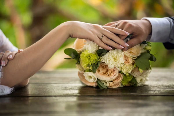 新娘和新郎的手放在结婚花束上 婚戒在焦点 木桌上的花束 横向框架 — 图库照片