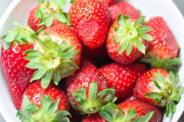 Taze organik çileklerin fotoğraf çekimi. Ayrıca gri ahşap dokular ve beyaz bir kase içeriyor. Parlak renklerin birleşimi öne çıkıyor.