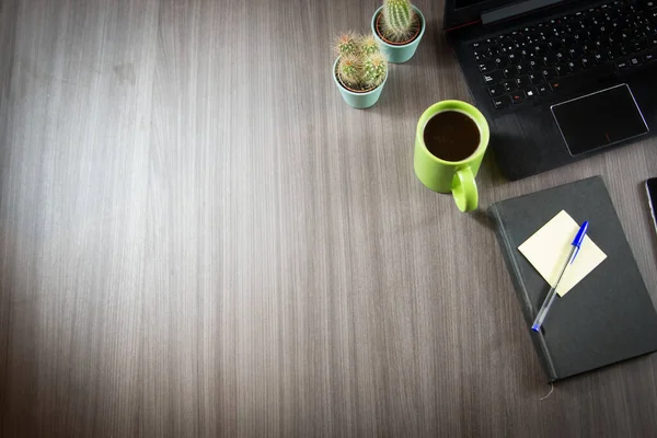Bilgisayarlı ve ofis aletli çalışma masası. Cep telefonu, not kağıtları, dizüstü bilgisayar, kalem, kaktüs, kahve ve yapraklar..