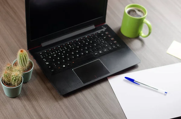 Bilgisayarlı ve ofis aletli çalışma masası. Cep telefonu, not kağıtları, dizüstü bilgisayar, kalem, kaktüs, kahve ve yapraklar..