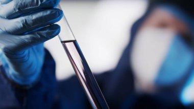  Kapatın. Koruyucu takım elbiseli laboratuvar asistanı laboratuvar cam cuvette numunesi üzerinde çalışıyor..