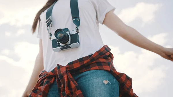 Young woman with a vintage camera and outstretched hands enjoying the breeze. Low angle shot with blue sky with clouds on background