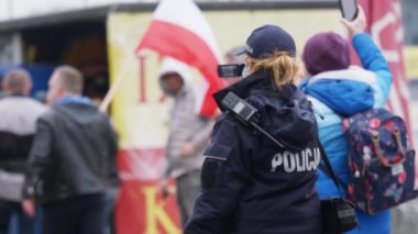 Varşova, Polonya 04.15.2020 - Girişimcilerin protestosu, genç bayan polis memuru protestoyu kaydediyor. Sokağa çıkma yasağının ortasındaki kalabalığın içinde koruyucu yüz maskesi ile.
