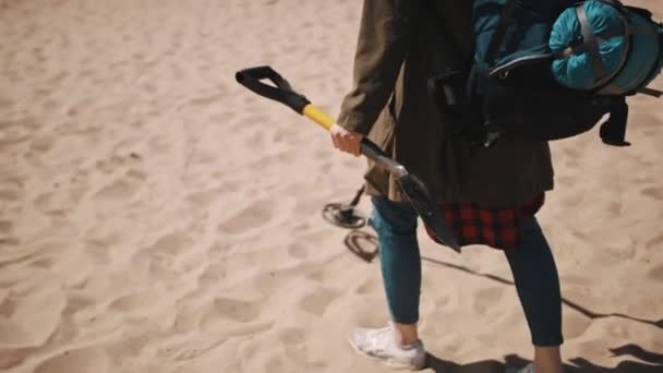 Vrouw met de schop en rugzak die zand zoekt met de metaaldetector. Schatzoeken op het zandstrand. — Stockvideo