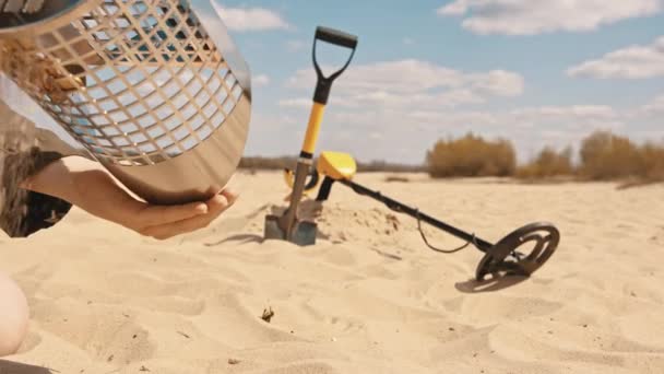 Mann nimmt Münzen aus dem Siebsandschöpfer. Suche nach Edelmetallen am Sandstrand — Stockvideo