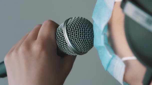 Jovem cantora cantando no microfone fith máscara facial em estúdio em casa. Trabalho remoto, auto-isolamento e prevenção da propagação do coronavírus — Vídeo de Stock