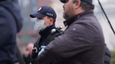 Varşova, Polonya 04.15.2020 - Girişimcilerin protestosu, sokağa çıkma yasağının ortasında halkın arasında koruyucu maskeli genç polis