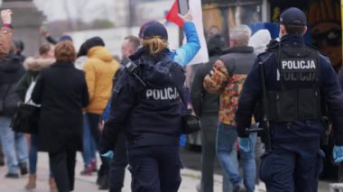 Varşova, Polonya 04.15.2020 - Girişimcilerin protestosu, genç bayan polis memuru protestoyu kaydediyor. Sokağa çıkma yasağının ortasındaki kalabalığın içinde koruyucu yüz maskesi ile.