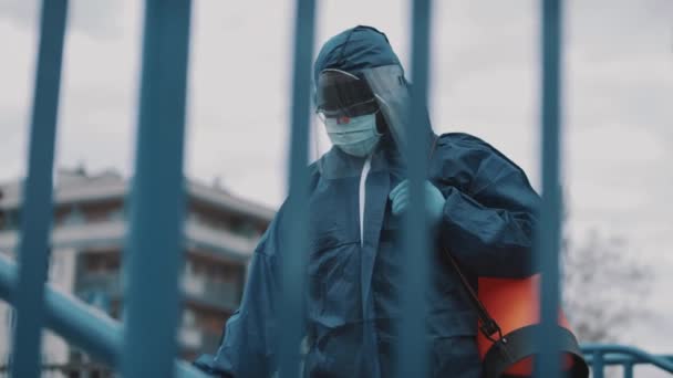 Kék védőruhát viselő személy, aki fertőtleníti a közösségi teret — Stock videók