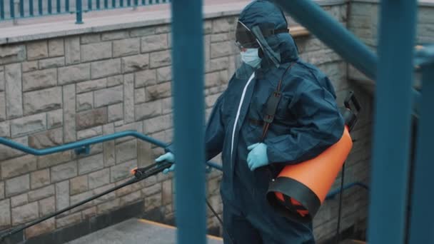 Homem com terno de proteção NBC, máscara, óculos de proteção facial, desinfecta escadas — Vídeo de Stock