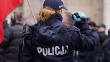 Varşova, Polonya 04.15.2020 - Girişimcilerin protestosu, genç bayan polis memuru protestoyu kaydediyor. Sokağa çıkma yasağının ortasındaki kalabalığın içinde koruyucu yüz maskesi ile.