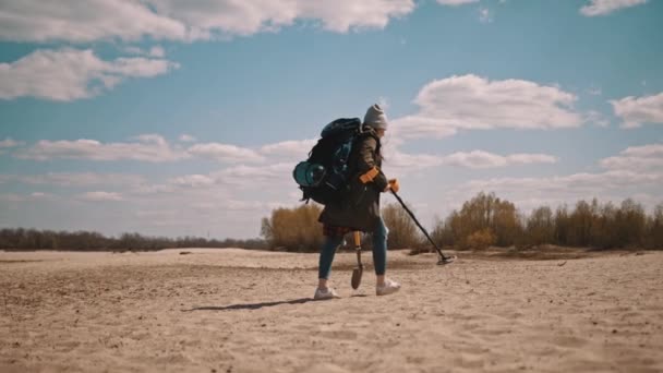 Nierozpoznawalna kobieta z wykrywaczem metalu szukająca artefaktów spacerujących po piaszczystej plaży w słoneczny dzień — Wideo stockowe