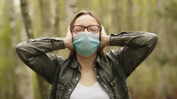 Självisolering och att fly det dagliga rutinkonceptet. Ung kvinna med facemask som täcker öronen i skogen. — Stockvideo