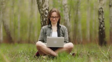 Doğada dizüstü bilgisayar kullanan genç bir kadın. Uzak çalışma veya uzaklık öğrenme kavramı