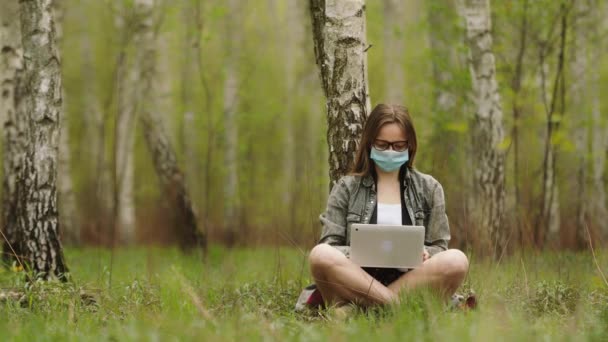 Freiberufler während der Quarantäne in der Natur. Frau mit Maske arbeitet im Wald an Laptop — Stockvideo