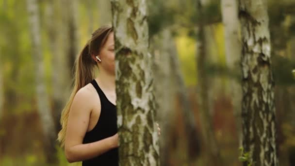 Gesunder Lebensstil. Junge Kaukasierin mit kabellosen Kopfhörern läuft im Wald. — Stockvideo