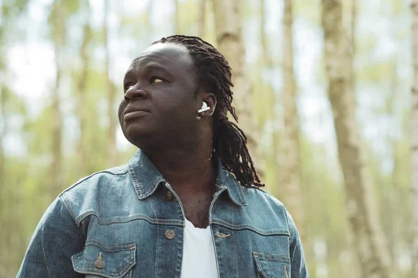 Portrét afrického muže s bezdrátovými sluchátky v lese, jak se dívá přes rameno. Kopírovat prostor — Stock fotografie