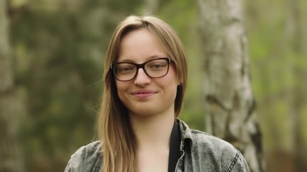 Porträtt av en ung kacasiansk kvinna med glasögon som ler och nickar i parken — Stockvideo