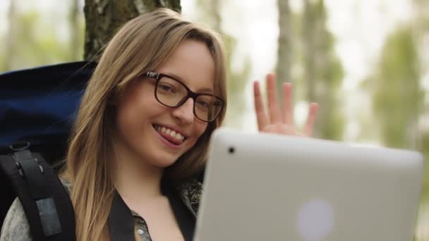 Jeune fille caucasienne avec des lunettes et sac à dos se reposant dans la nature et ayant un appel vidéo avec la famille et les amis — Video