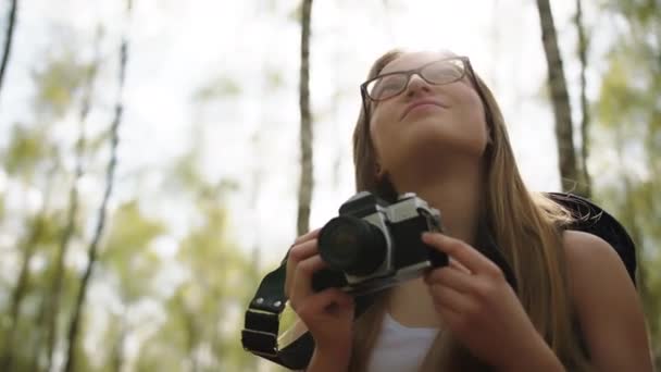 Donna sorridente caucasica con fotocamera vintage godendo di vacanza nella natura. Zaino in spalla nella foresta. Riflesso delle lenti — Video Stock